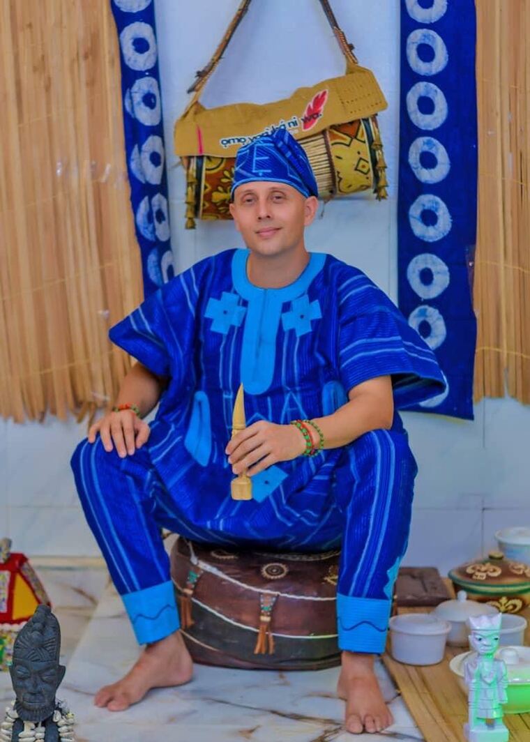 Yisel Ifálàdé sentado, con atuendo yorùbá, junto a su bolsa de Ọmọ Yorùbá Ni Wa